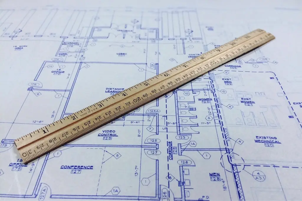 A blueprint sheet with a wooden ruler lying across it, the drawing a bill of quantities is measured from