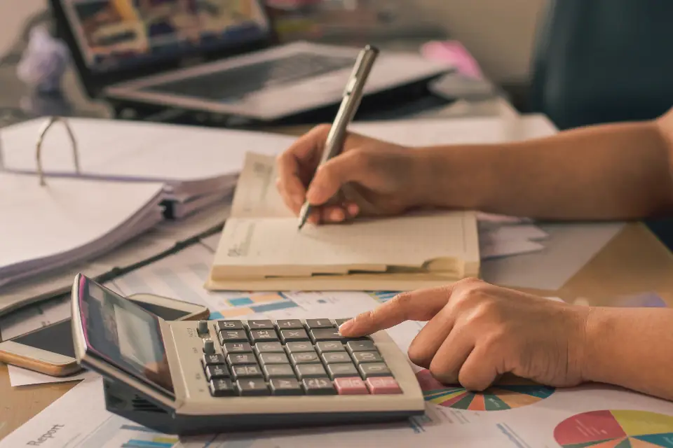 Hands working through figures with a calculator and a ledger