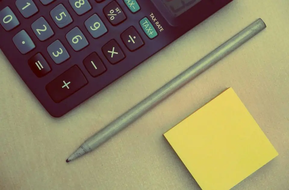 A calculator, a pencil and a sticky note on a desk, the tools of a rate typed from memory