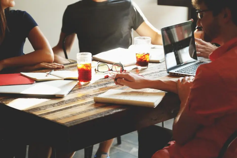 A small team working around a wooden table with notebooks, a studio-sized practice rather than an enterprise
